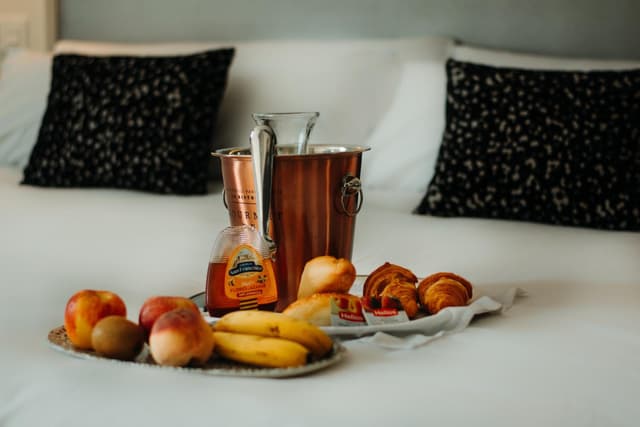 Breakfast spread on a bed with fruit, pastries, honey, and a copper ice bucket.