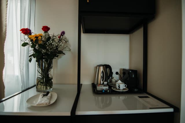 Hotel room beverage station with electric kettle, coffee machine, and vase of flowers.