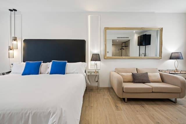 Hotel room with a white bed, blue pillows, and a beige sofa.