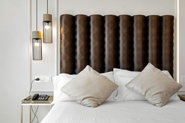 Hotel bedroom with a bed featuring white linens and a brown padded headboard.