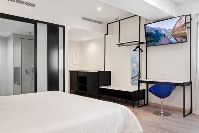Hotel room with a white bed, dark wood furniture, and a wall-mounted television.