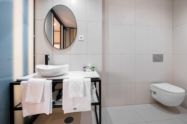 Bathroom with a white vessel sink, black metal vanity, and wall-mounted toilet.