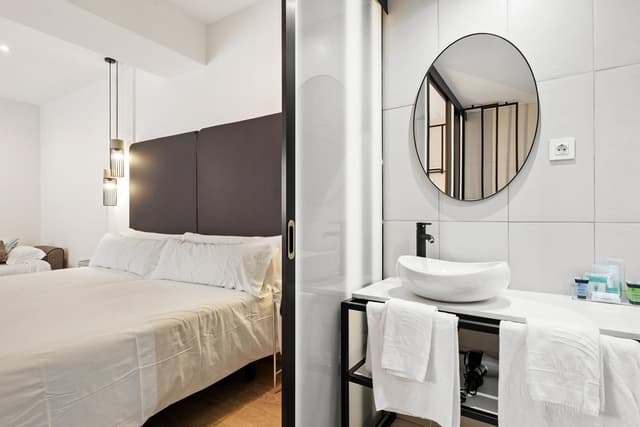 Hotel room with a bed and a bathroom vanity with a round mirror.