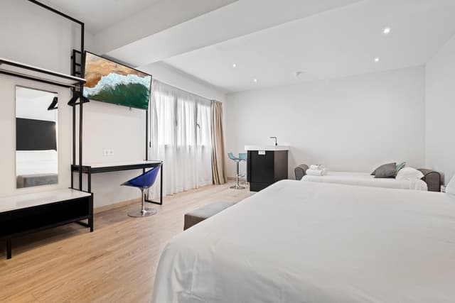 Hotel room with two white beds, a desk with a blue chair, and a wall-mounted television.