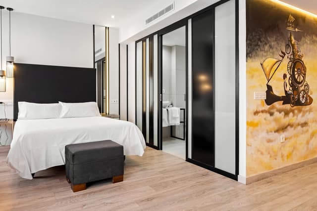 Hotel room with a white bed, black headboard, and a colorful steampunk wall mural.