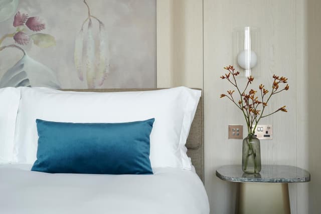 white bed with blue pillows and a vase of flowers