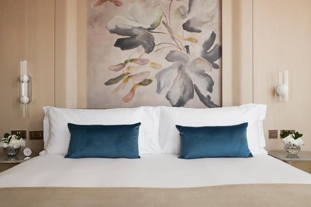 white bed with blue pillows and a painting on the wall