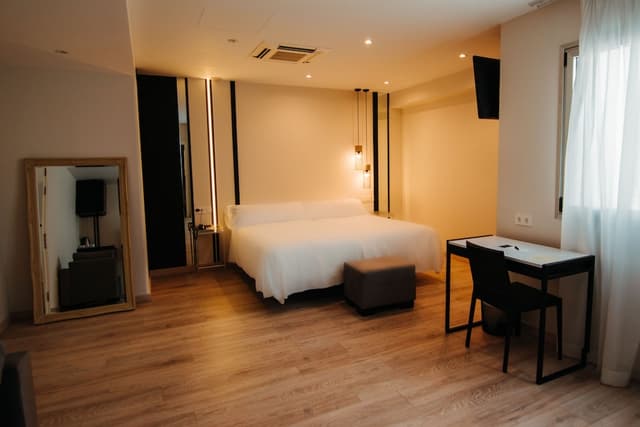 Hotel room with a white bed, black desk, and light wood flooring.